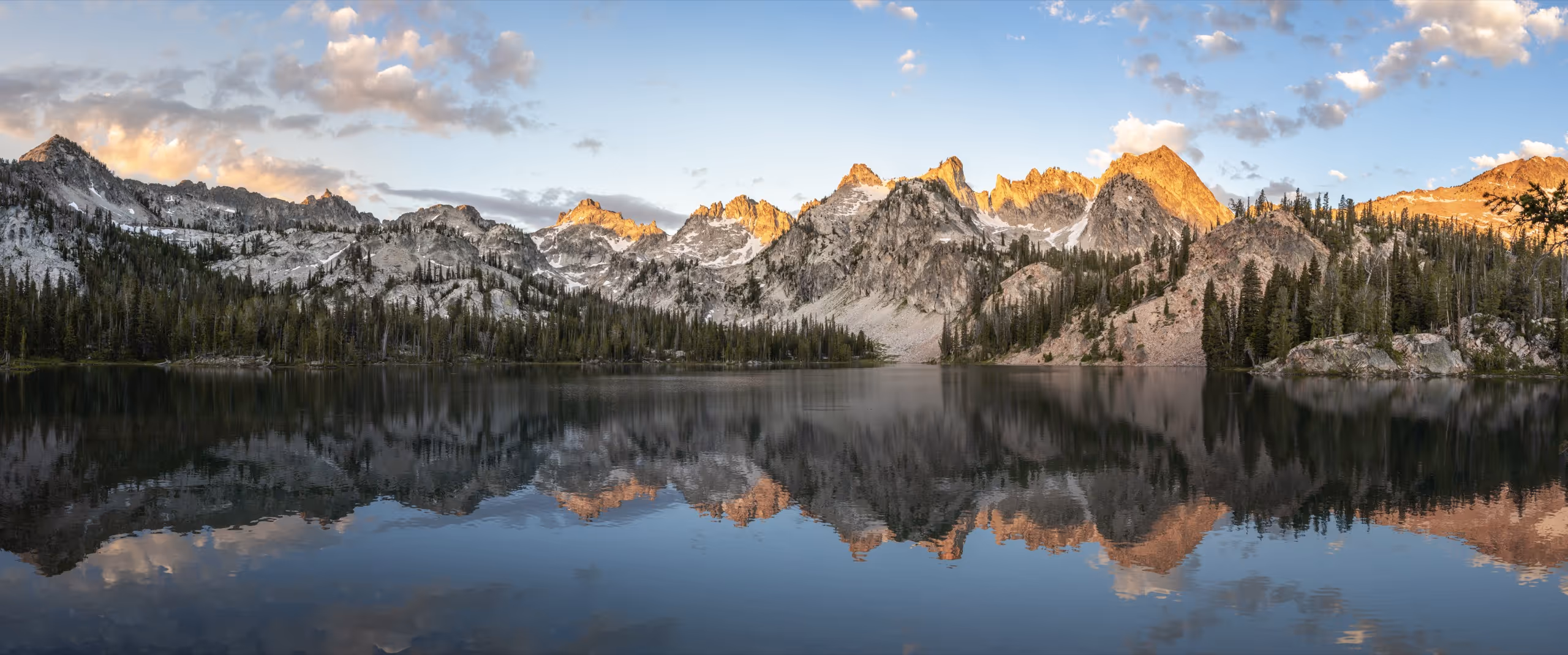 A still alpine lake mirroring the Sawtooth peaks at sunrise in Amelia County, Idaho.