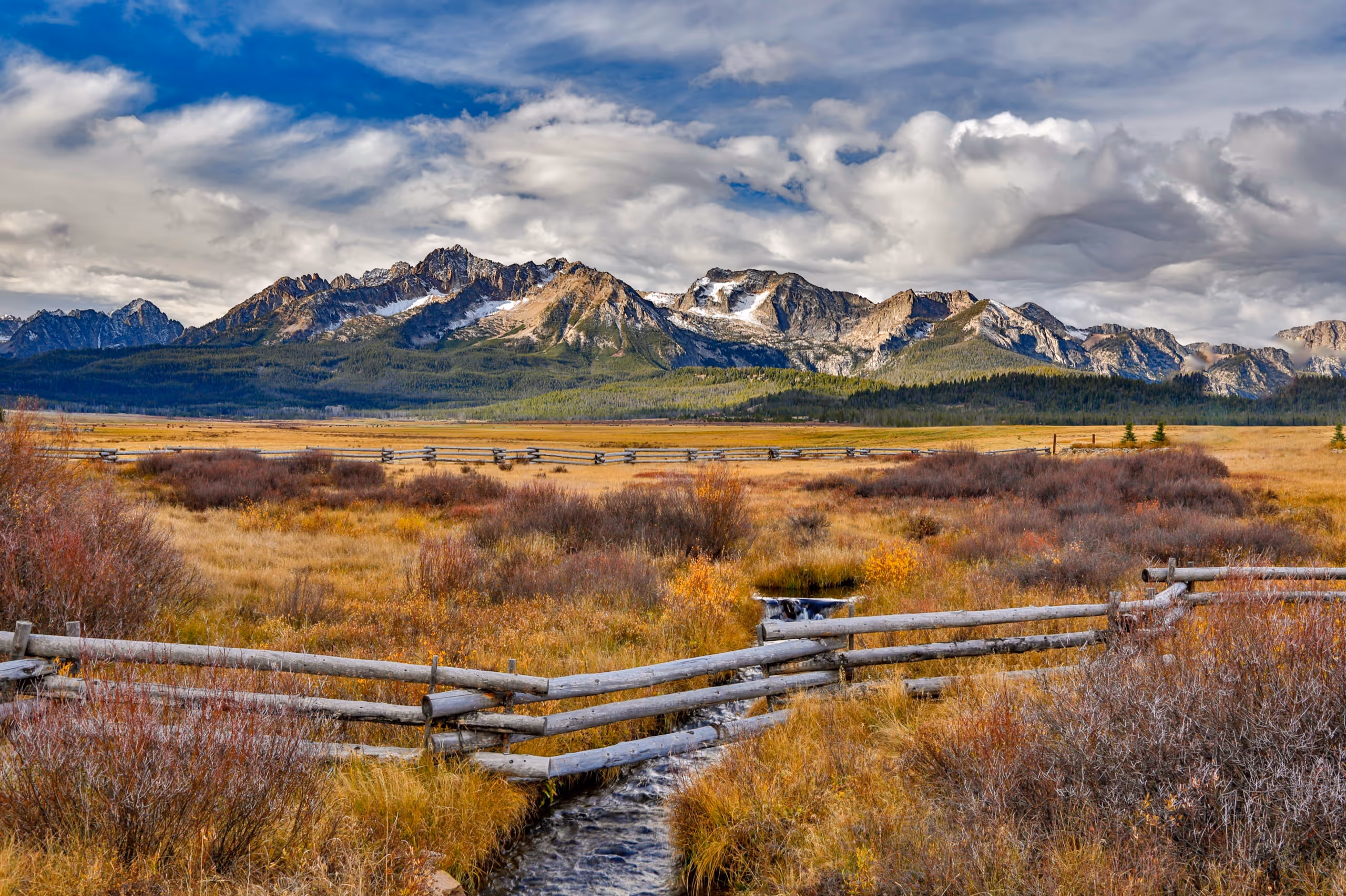 The Sawtooth Range over a golden meadow and log fence in Amelia County, Idaho.